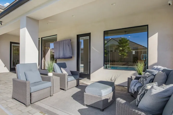 Expansive covered patio featuring recessed lighting, a paver stone surface, large black-framed windows, and direct access to a pool area