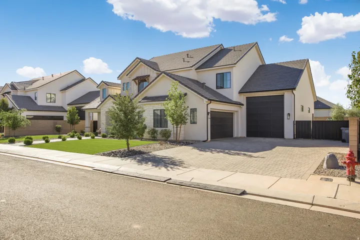 Stucco exterior with dark trim accents, a paver driveway, an attached two-car garage, and mature landscaping