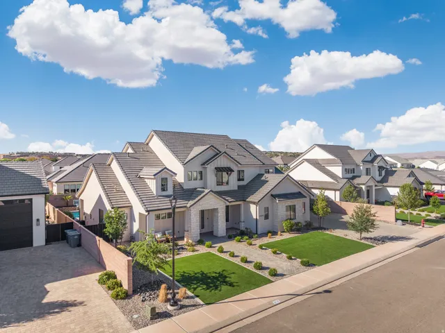 Modern exterior with a light stucco finish, stone accents, dark trim, a gabled roof, and a paver driveway