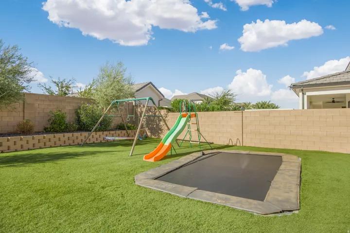 Expansive backyard featuring artificial turf, a block privacy fence, and a tiered retaining wall with integrated landscaping