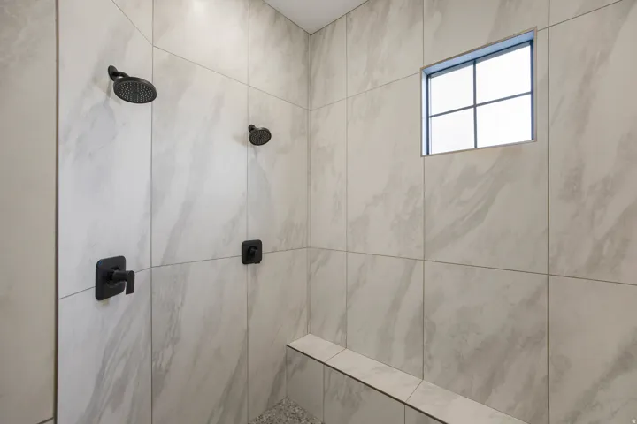 Walk-in shower with large format tile, dual matte black showerheads, built-in bench, and pebble-finish shower pan