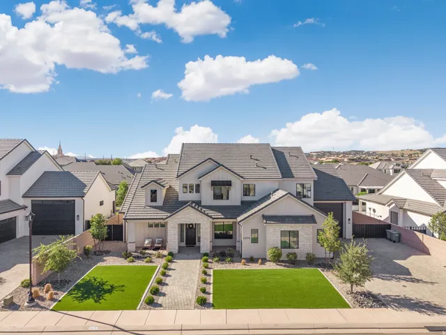 Modern facade featuring a stone and stucco exterior, dark roof tiles, a paver walkway, and artificial turf landscaping