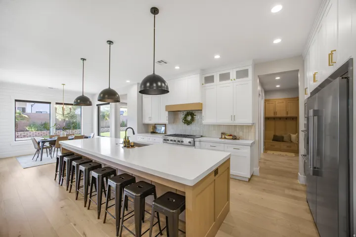 Expansive kitchen island with seating, white shaker cabinetry, stainless steel appliances, and light wood-finish flooring