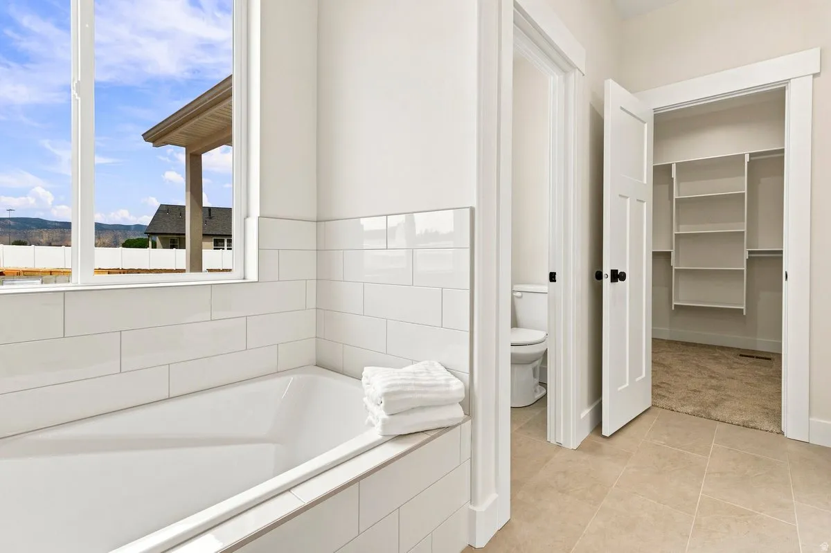 Recessed bathtub with white subway tile surround, white trim window, and ceramic floor tile