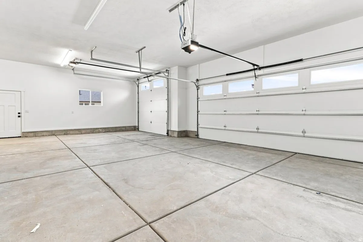 Spacious garage with concrete flooring, overhead lighting, and two white overhead garage doors with window inserts