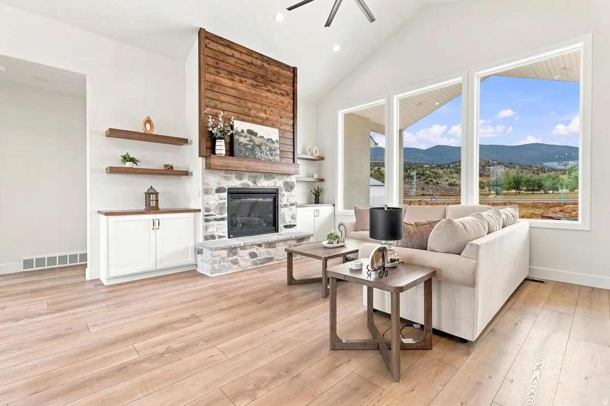 Vaulted ceiling, stone fireplace with wood mantel and surround, built-in cabinetry with wood countertops, wood-finish flooring, and expansive windows