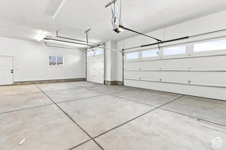 Spacious garage with concrete flooring, overhead lighting, and two white overhead garage doors with window inserts