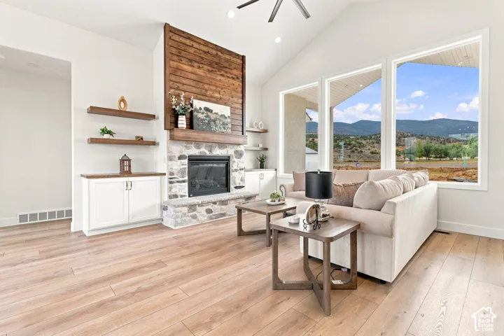 Vaulted ceiling, stone fireplace with wood mantel and surround, built-in cabinetry with wood countertops, wood-finish flooring, and expansive windows