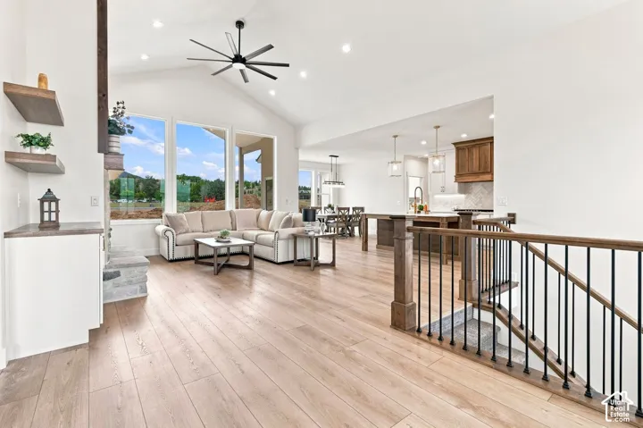 Vaulted ceilings with recessed lighting, wood-finish flooring, a stone-clad fireplace, built-in shelving, and a wood and metal stair railing