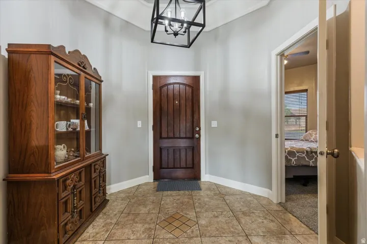 Wood-paneled entry door, tiled flooring with accent inlay, and vaulted ceiling with a geometric pendant light fixture