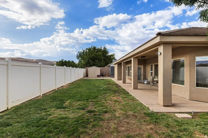 Expansive backyard featuring a covered patio, stucco exterior, privacy fencing, and a storage shed