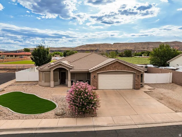 Stone veneer facade, attached garage, tile roof, desert-style landscaping with artificial turf, and a concrete driveway