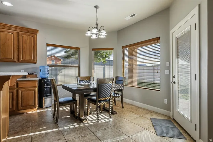 Tiled flooring, warm wood cabinetry, multiple windows with blinds, a glass-paneled exterior door, and a ceiling-mounted light fixture