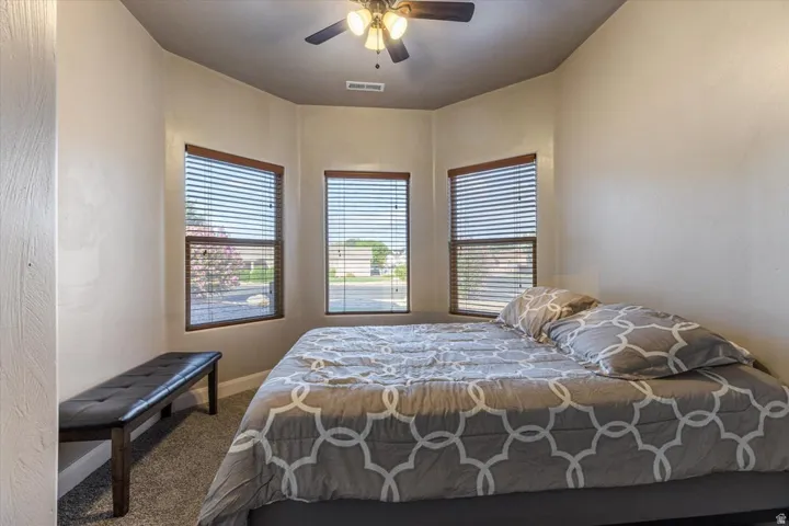 Carpeted room with a ceiling fan and a bay window featuring three individual windows