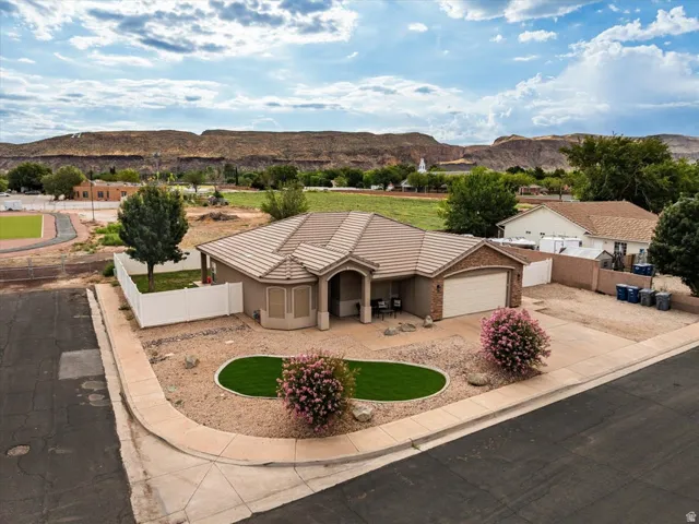 Single-story residence featuring a tile roof, an integrated two-car garage, and a low-maintenance front yard with artificial turf and mature plantings