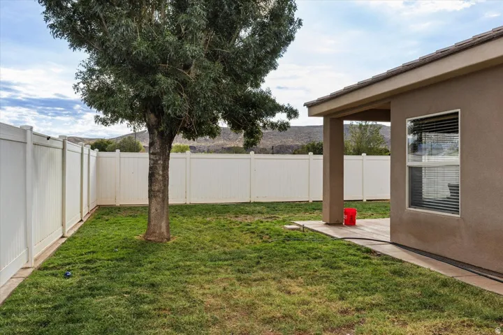 Expansive backyard featuring a mature tree, privacy fencing, and a covered patio area with a stucco exterior