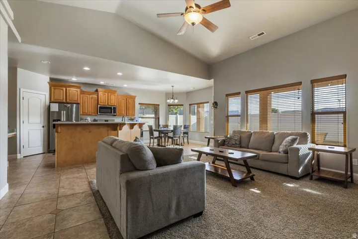 Vaulted ceilings, a ceiling fan, and multiple windows with horizontal blinds enhance this expansive living area