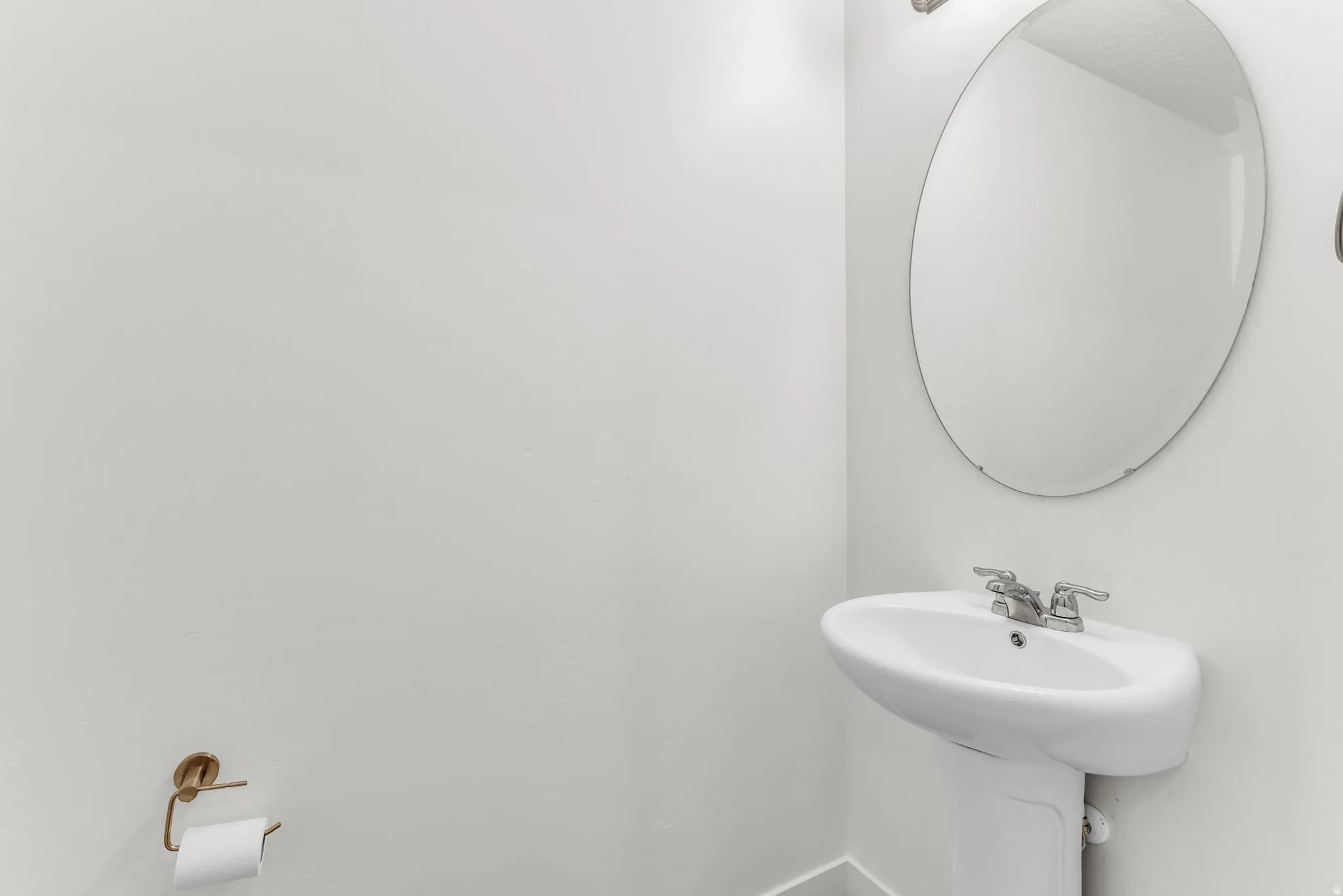 Pedestal sink with chrome fixtures and an oval wall mirror