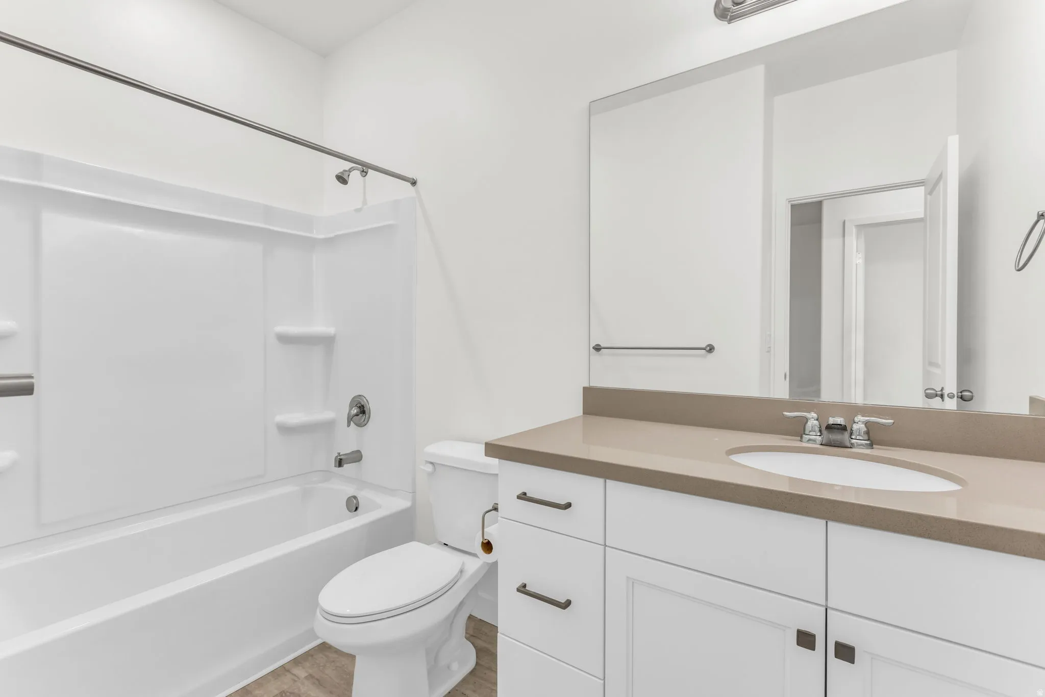 Integrated bathtub and shower with grab bar, white vanity with an undermount sink, light-colored countertop, and wood-finish flooring