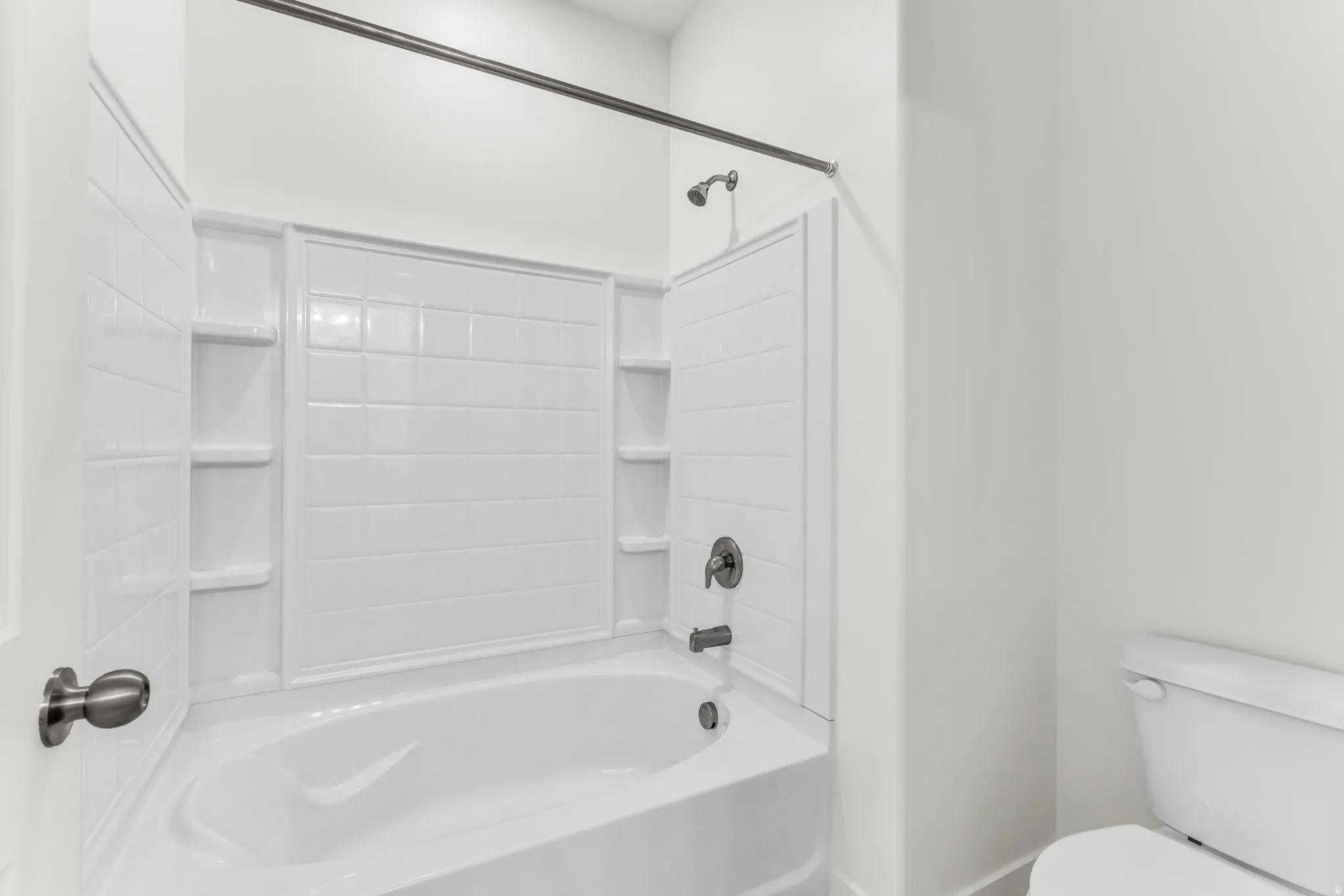 Bathtub with integrated shelving, matte black fixtures, and a white tiled shower surround