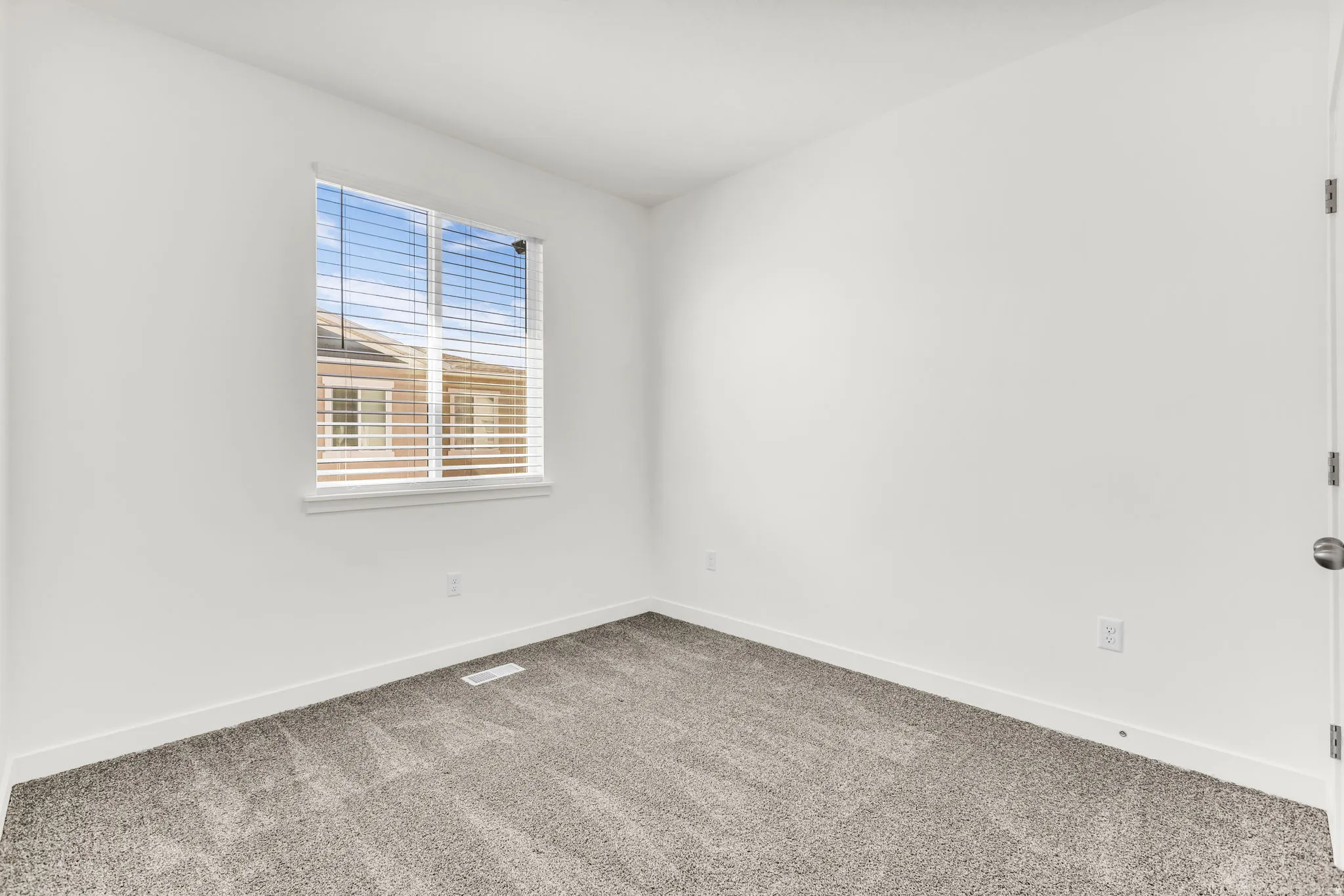 Recessed window with blinds, light gray carpet, white walls, and a white door with a round handle