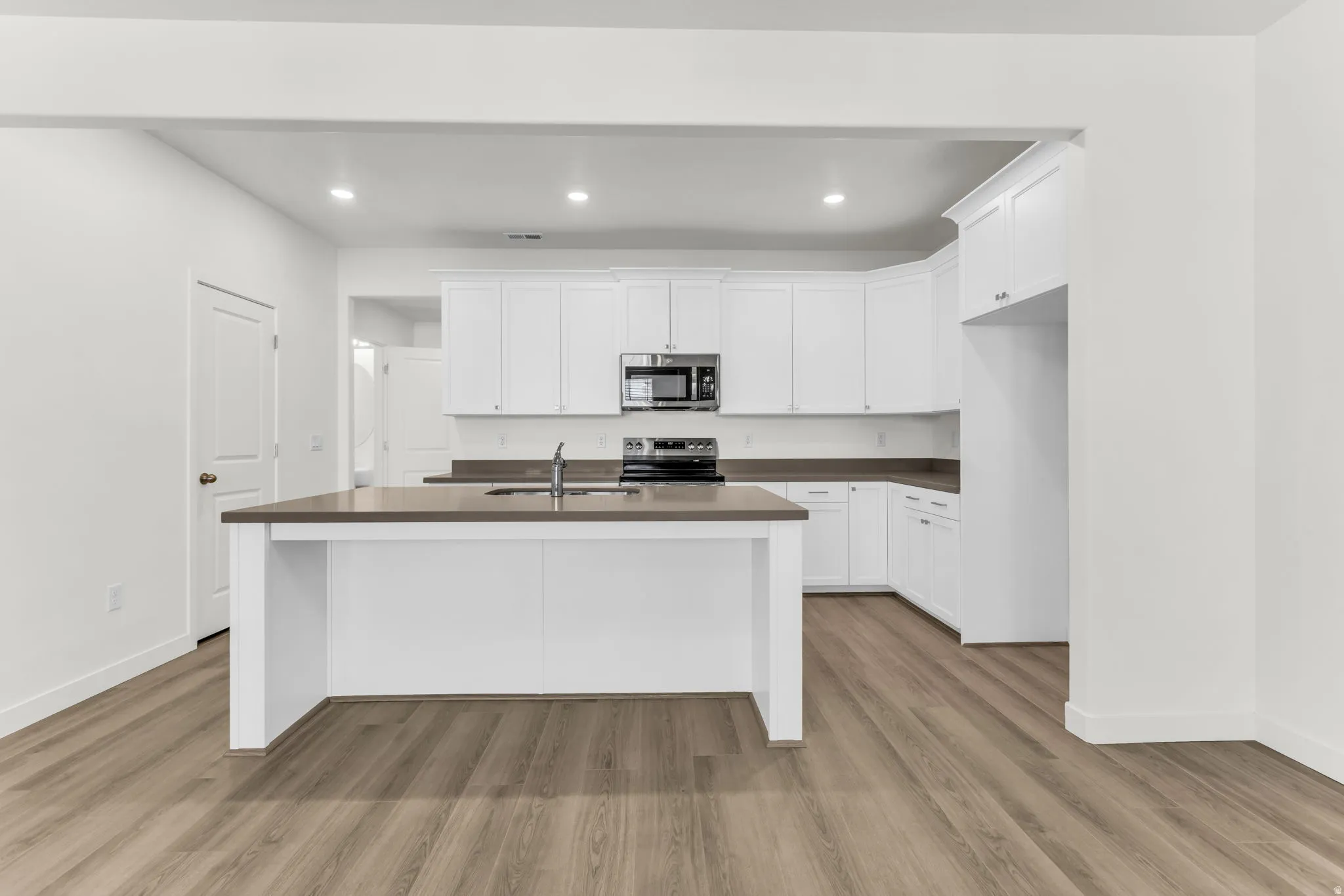 Kitchen featuring an expansive island with a sink, white cabinetry, dark countertops, and wood-finish flooring