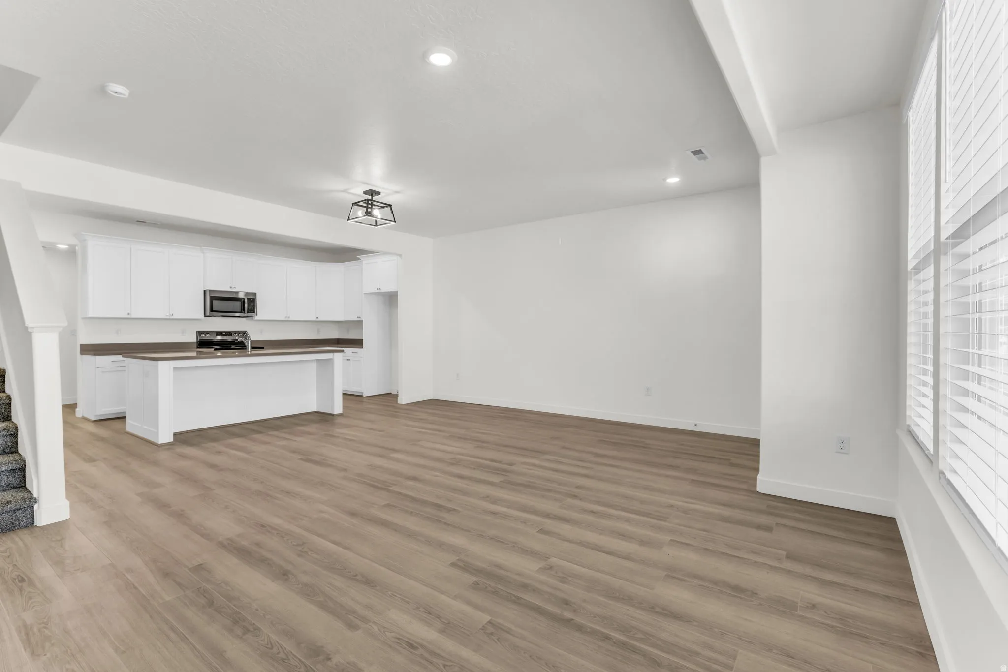 Open-concept living space with wood-finish flooring, white cabinetry, dark countertops, and stainless steel appliances