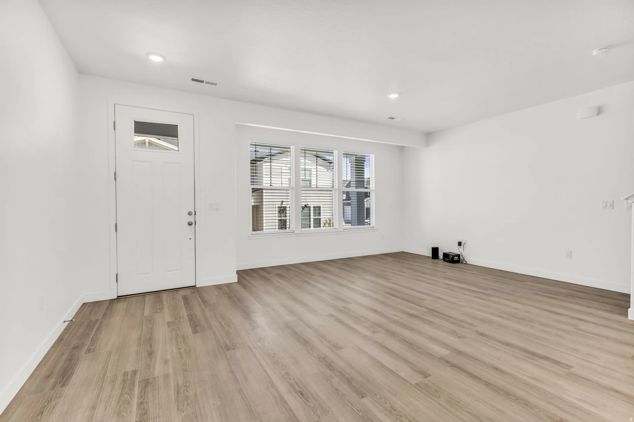 Wood-finish flooring, recessed lighting, white trim, and a multi-pane window with blinds