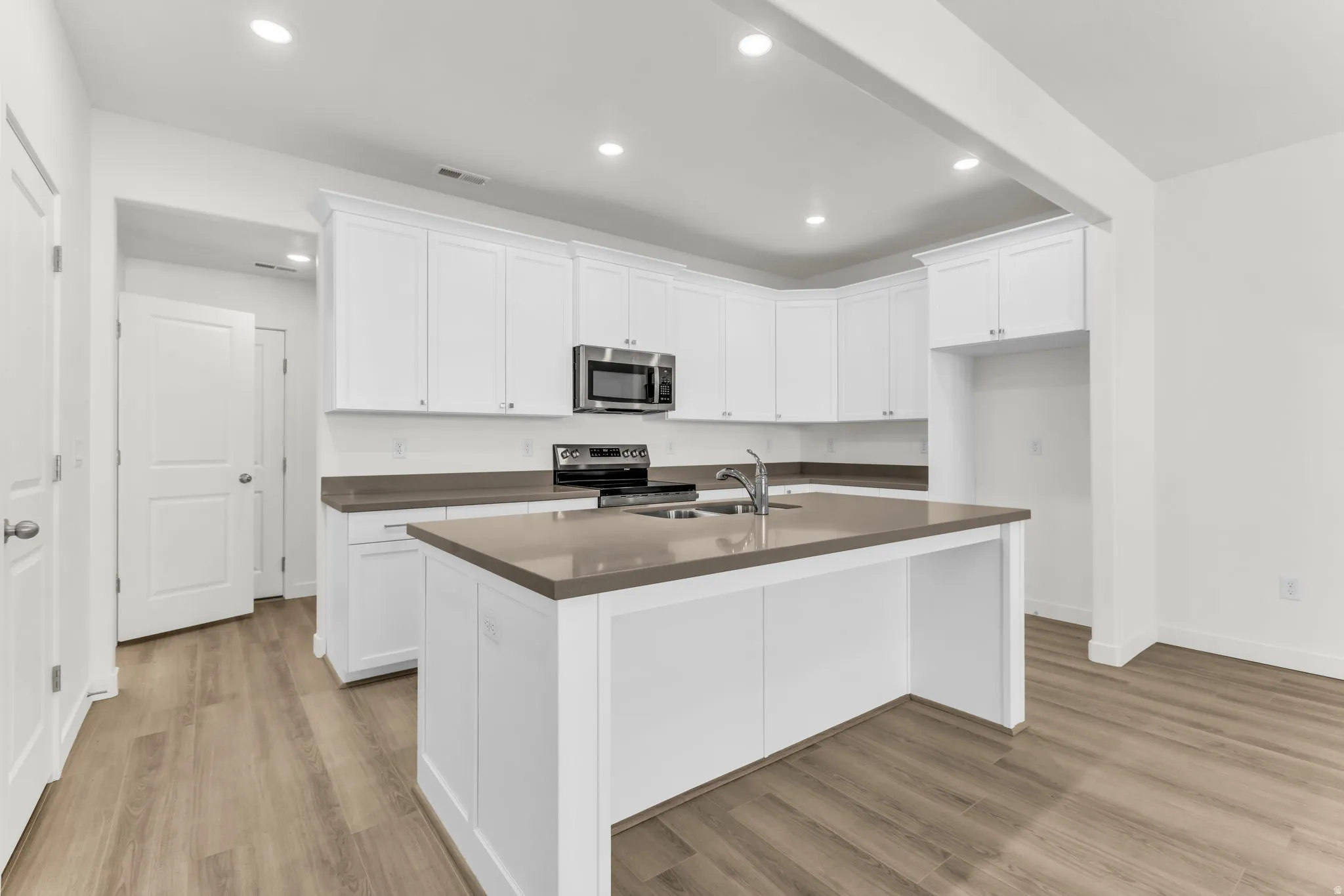 Kitchen featuring recessed lighting, white cabinetry, a central island with an undermount sink, stainless steel appliances, and wood-finish flooring