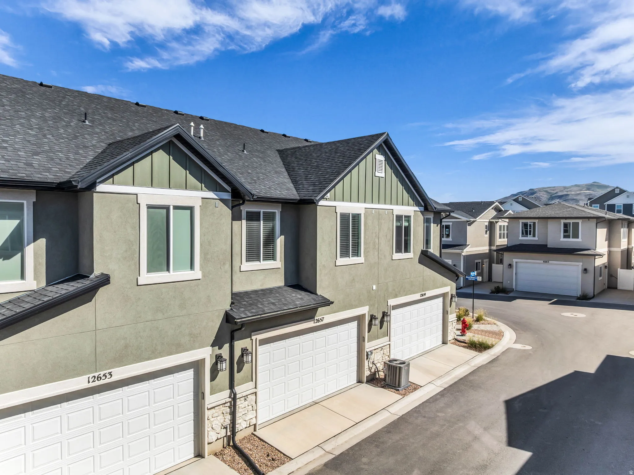 Stucco exterior with stone accents, dark asphalt shingle roof, white panel garage doors, and individual air conditioning units