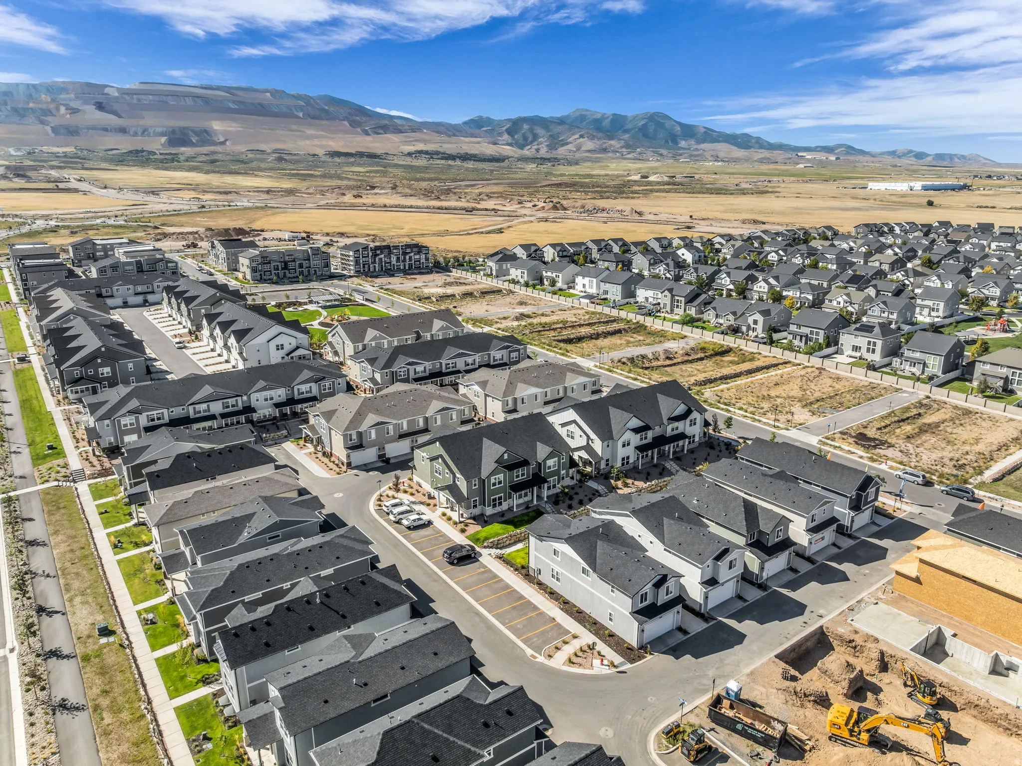 Expansive residential development with a mountain backdrop, featuring single-family homes and townhomes, paved streets, and undeveloped lots