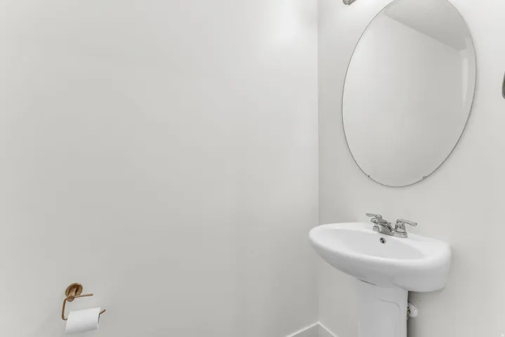 Pedestal sink with chrome fixtures and an oval wall mirror