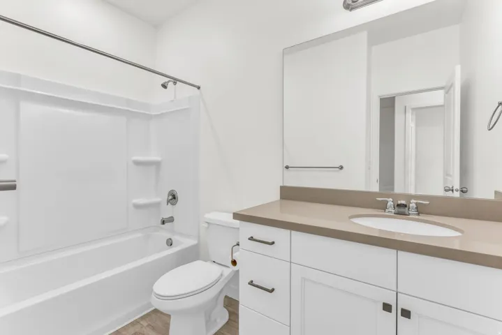 Integrated bathtub and shower with grab bar, white vanity with an undermount sink, light-colored countertop, and wood-finish flooring