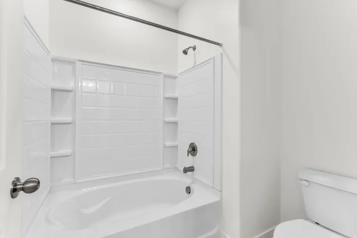 Bathtub with integrated shelving, matte black fixtures, and a white tiled shower surround
