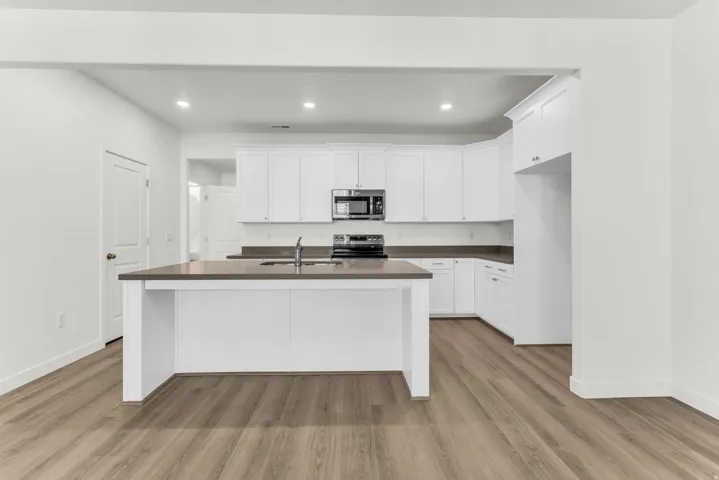 Kitchen featuring an expansive island with a sink, white cabinetry, dark countertops, and wood-finish flooring