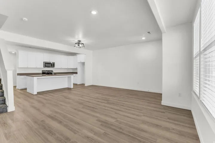 Open-concept living space with wood-finish flooring, white cabinetry, dark countertops, and stainless steel appliances