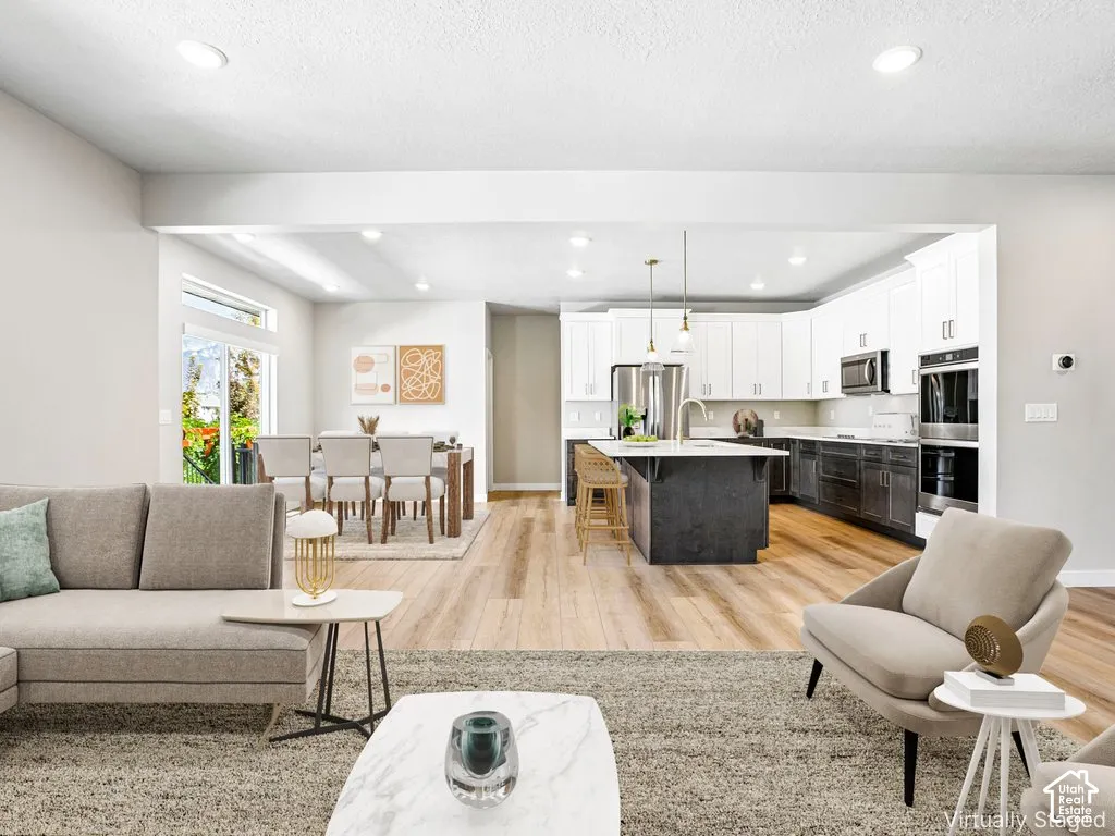 Open-concept living space featuring wood-finish flooring, recessed lighting, and a kitchen with white upper cabinetry and stainless steel appliances
