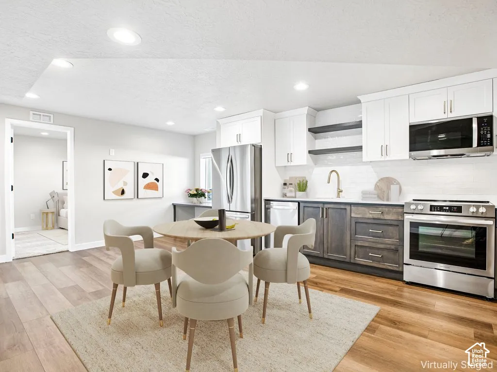 Open-concept kitchen with wood-finish flooring, two-tone cabinetry, stainless steel appliances, and recessed lighting