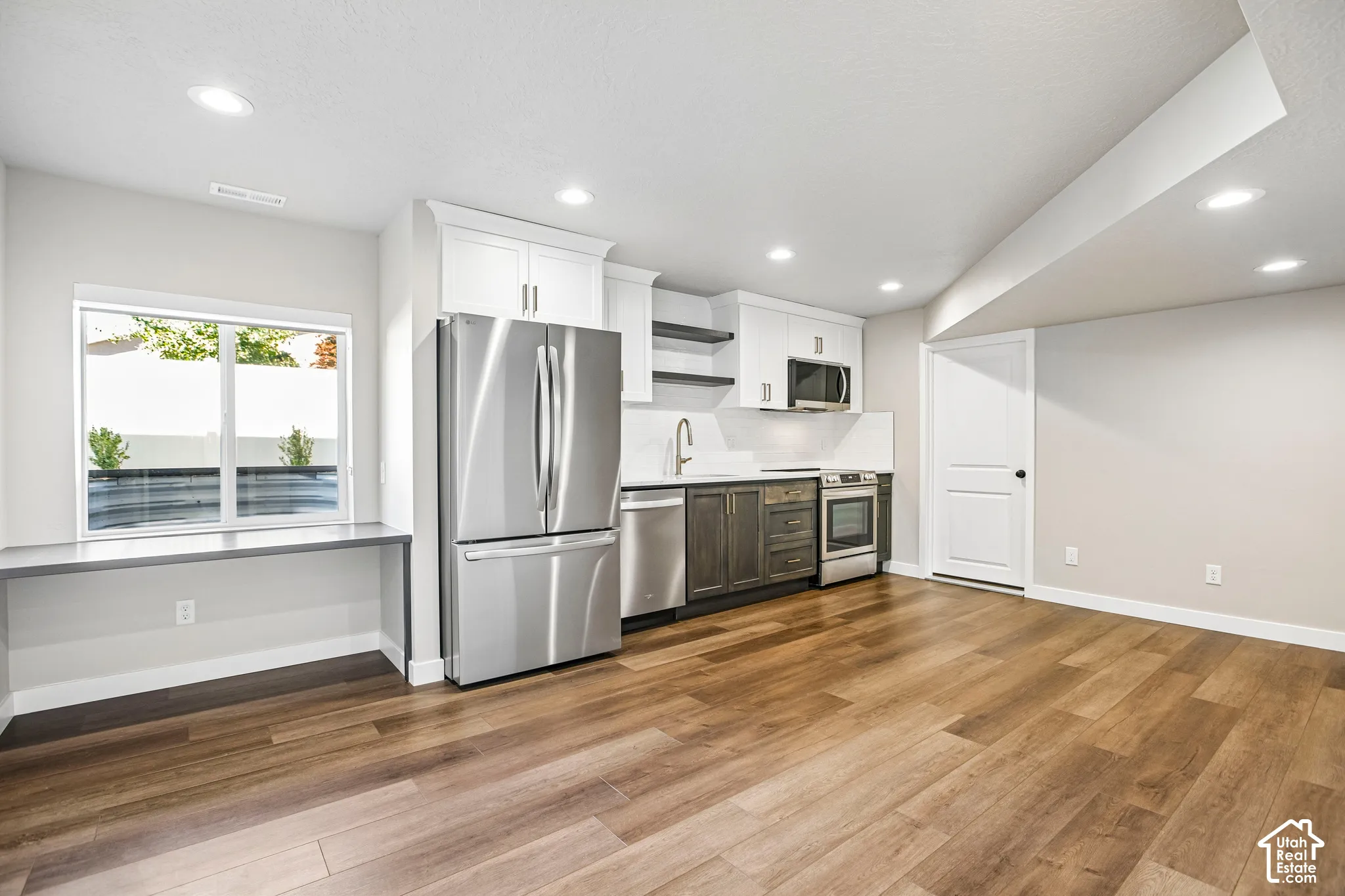 Wood-finish flooring with a modern kitchen featuring stainless steel appliances, white cabinetry, and a white backsplash