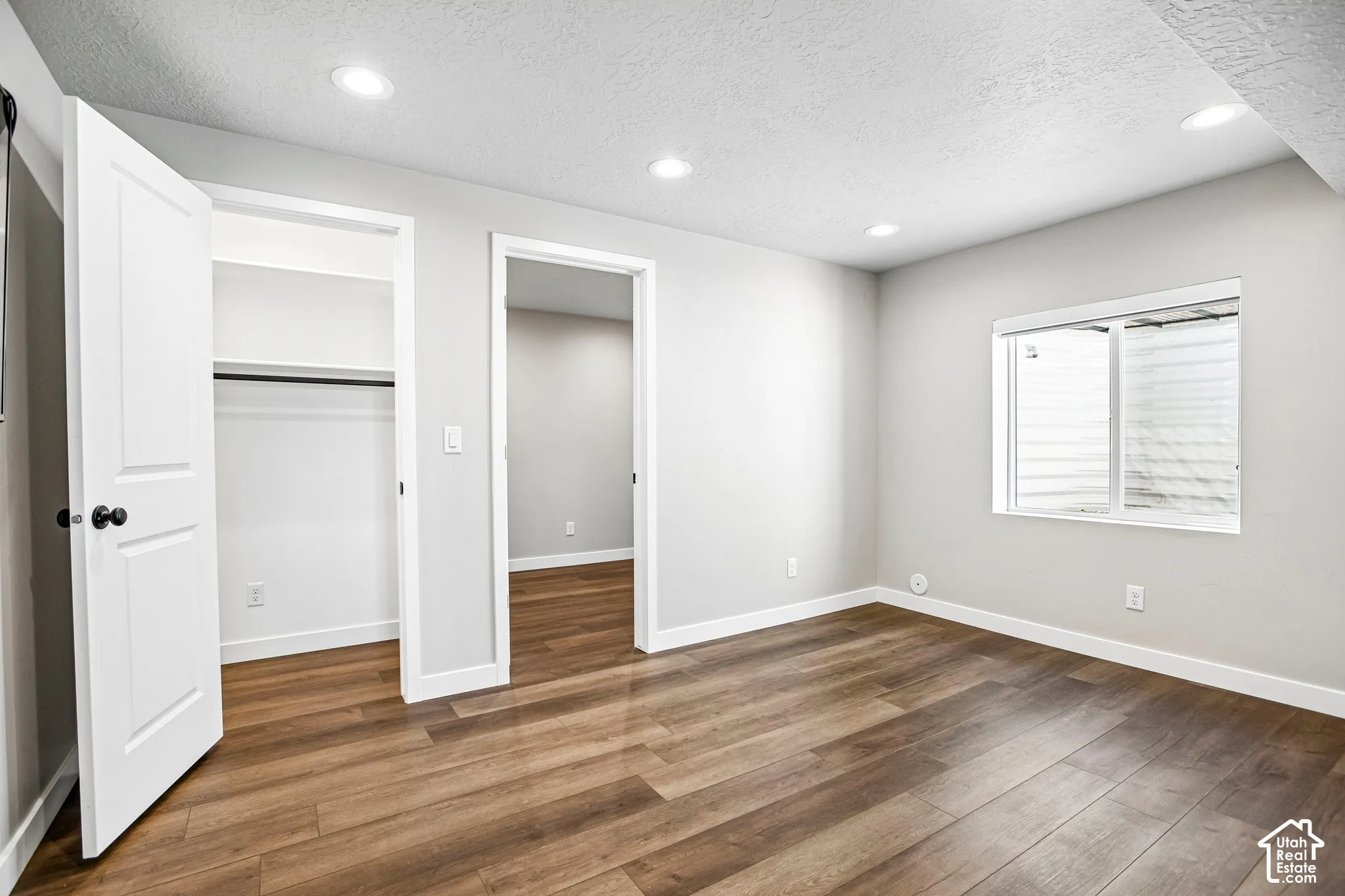 Recessed lighting, wood-finish flooring, white trim, and a built-in closet with shelving and hanging rod