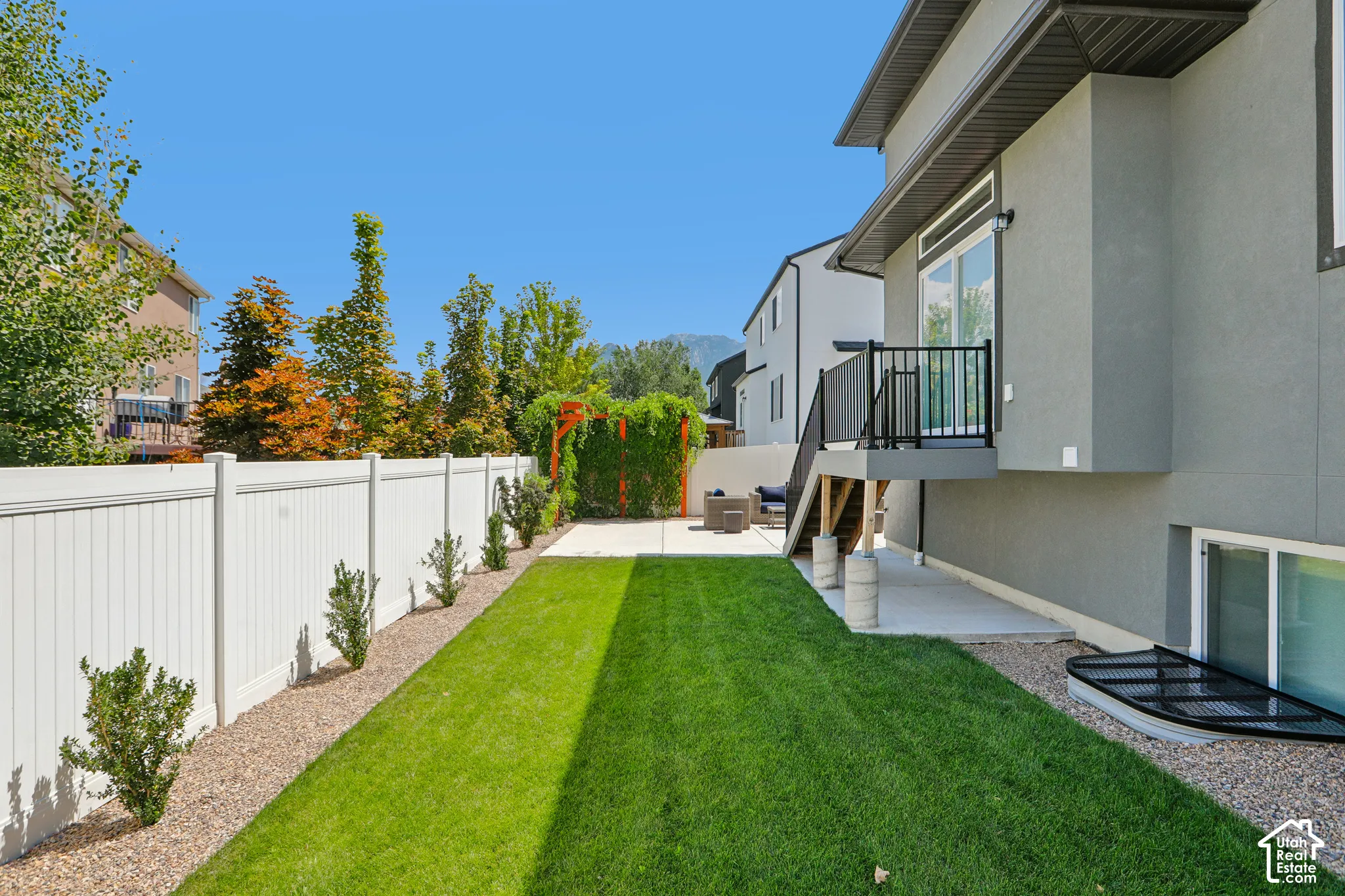 Expansive lawn area with a white privacy fence, concrete patio, and a second-story balcony with black railing