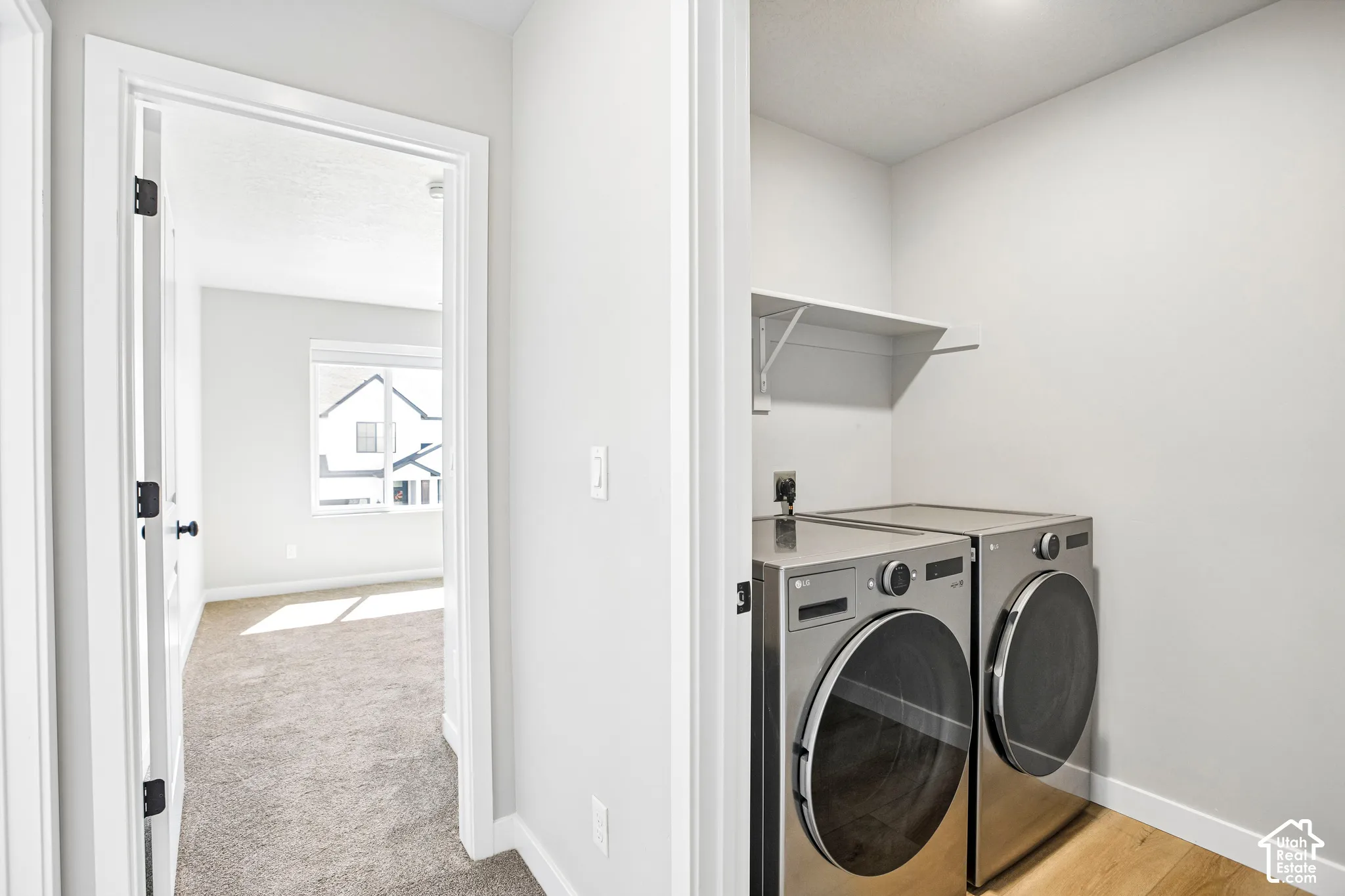 Dedicated laundry area featuring front-loading appliances, an overhead storage shelf, and wood-finish flooring
