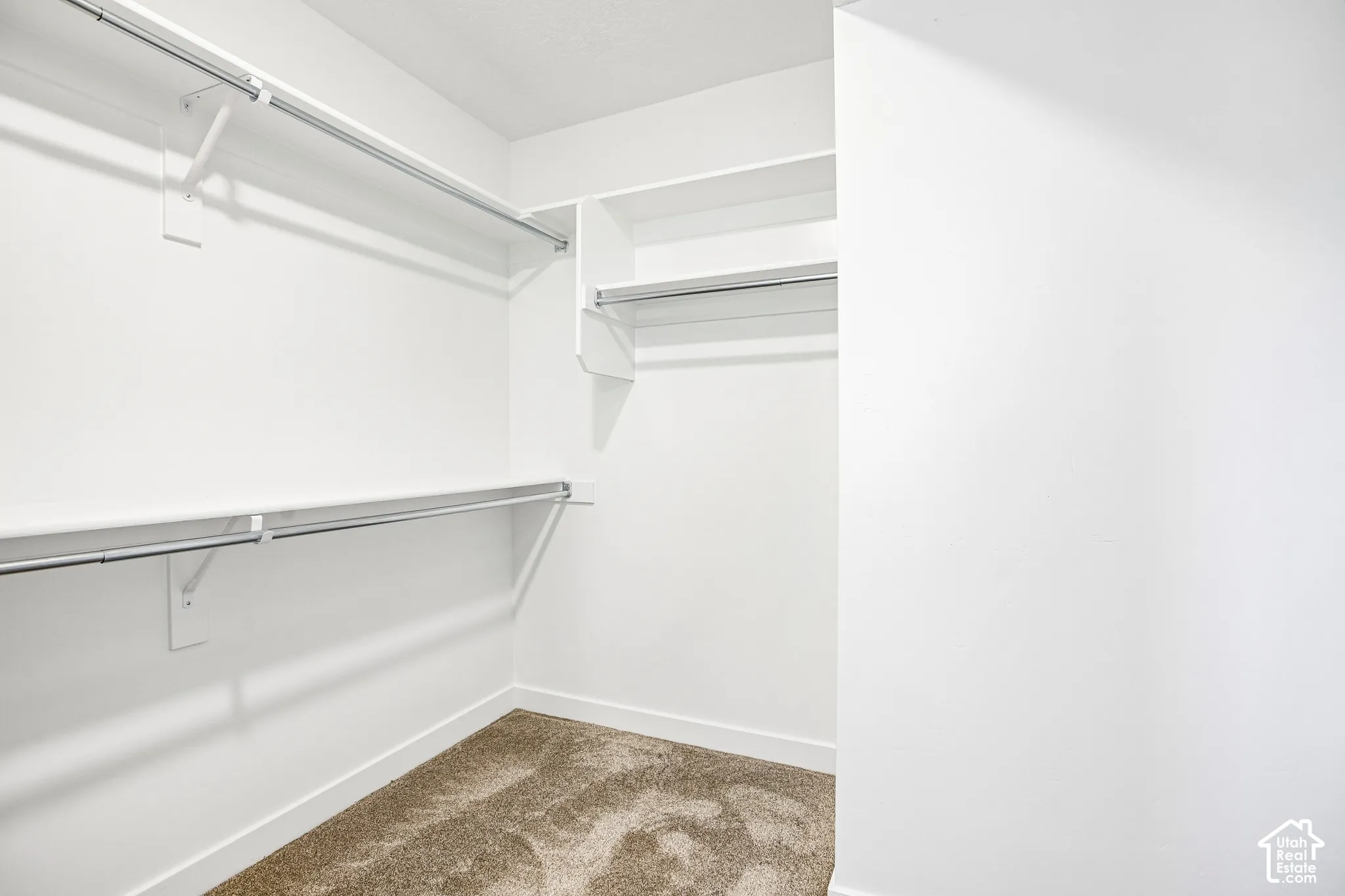Walk-in closet with multiple white wire shelving units and hanging rods, complemented by light-toned carpet flooring