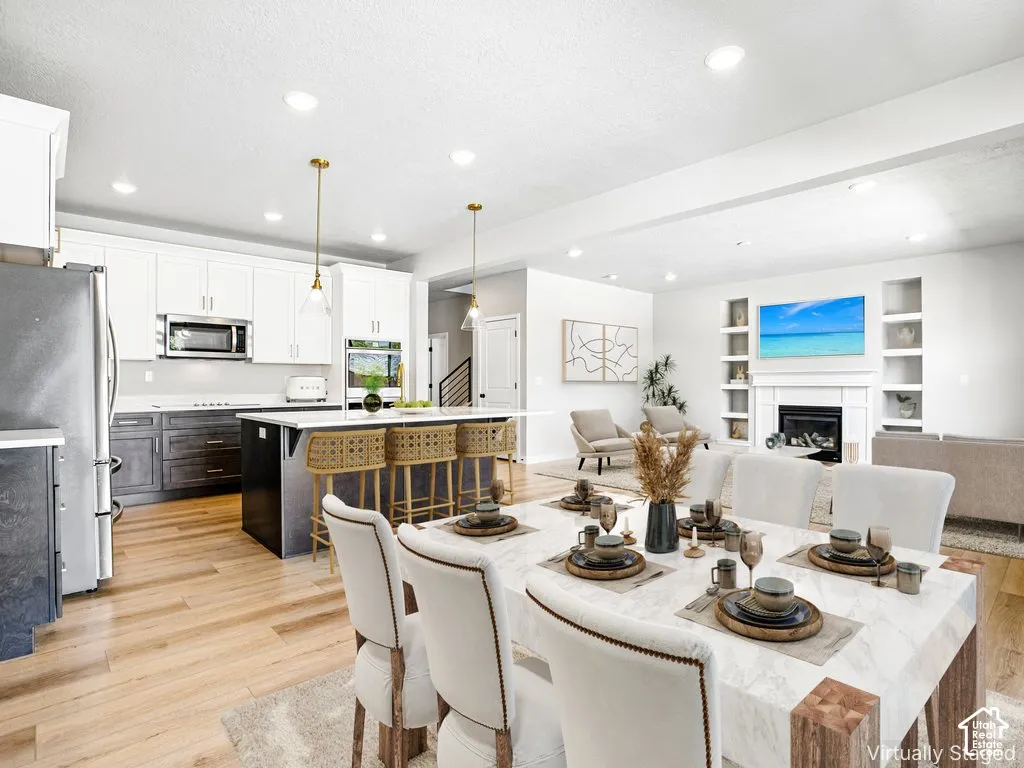 Open-concept living space with wood-finish flooring, a kitchen island, white cabinetry, recessed lighting, and a fireplace with built-in shelving