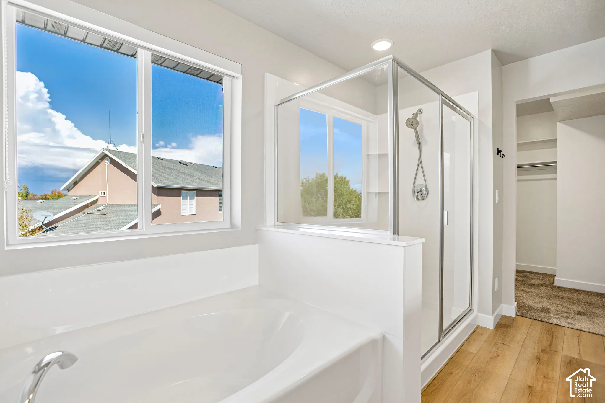 Built-in soaking tub, glass-enclosed shower, wood-finish flooring, and ample natural light