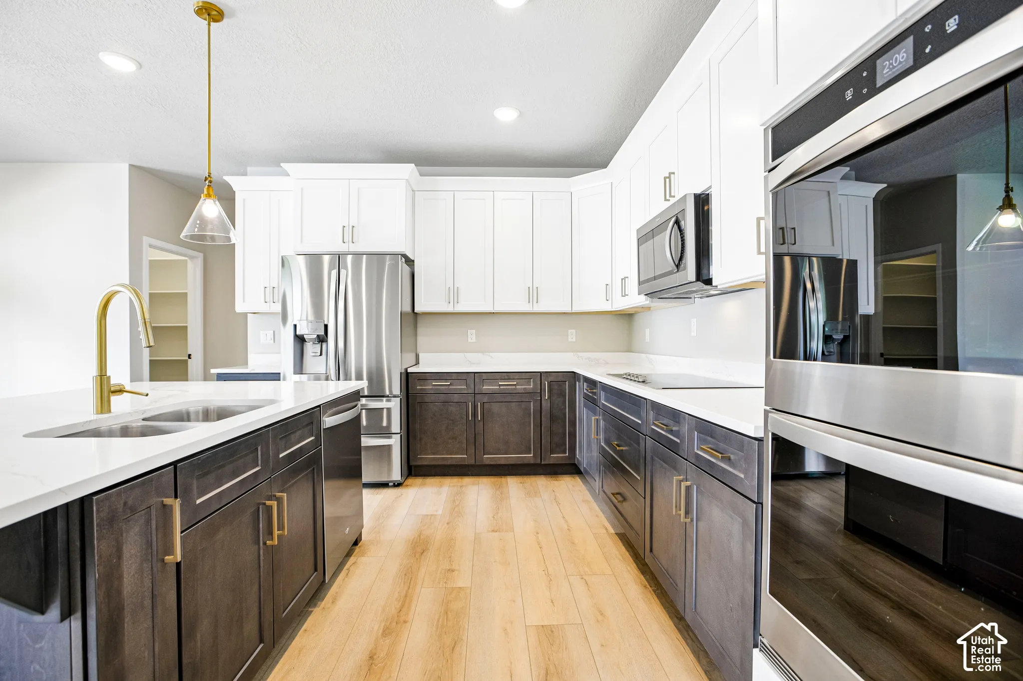 Gourmet kitchen featuring a gold-finish faucet, stainless steel appliances, wood-finish flooring, two-tone cabinetry, and recessed lighting