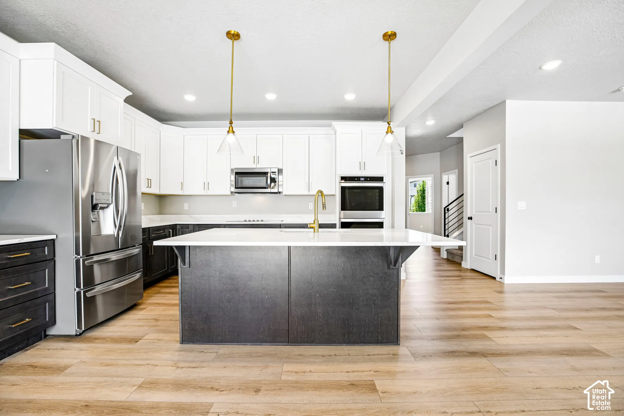 Spacious kitchen featuring an expansive center island, stainless steel appliances, dual-tone cabinetry, recessed lighting, and wood-finish flooring