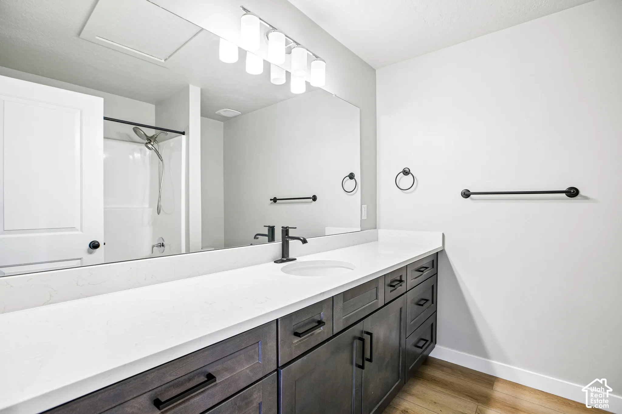 White countertop, dark wood-finish vanity with ample storage, large mirror, matte black fixtures, and wood-finish flooring