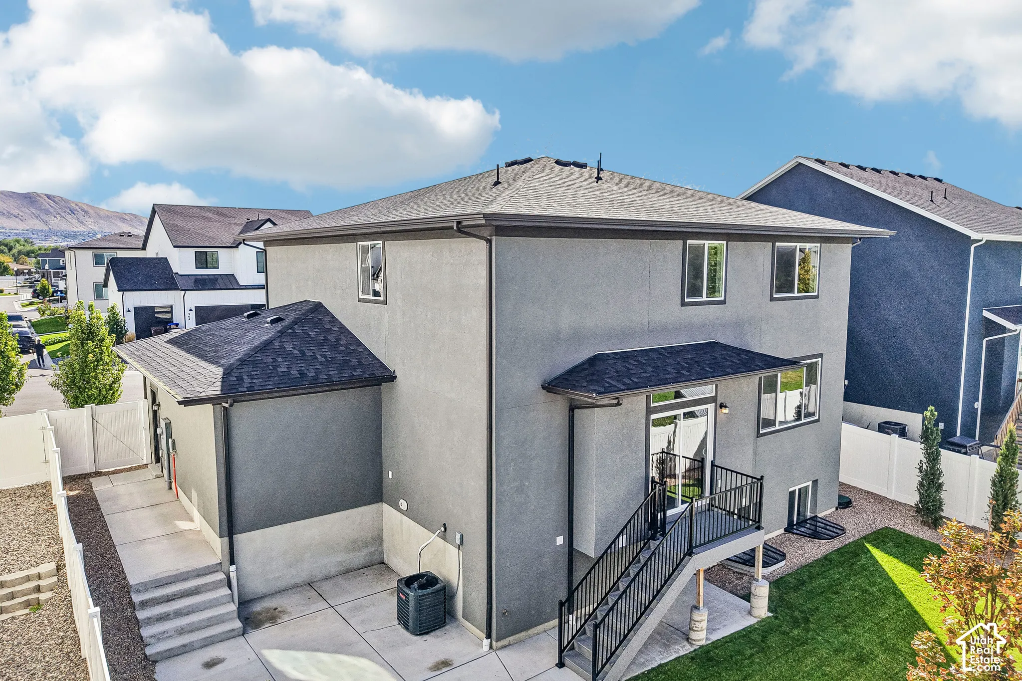 Stucco exterior with a multi-level concrete patio, private deck with metal railings, and a fenced yard with established lawn