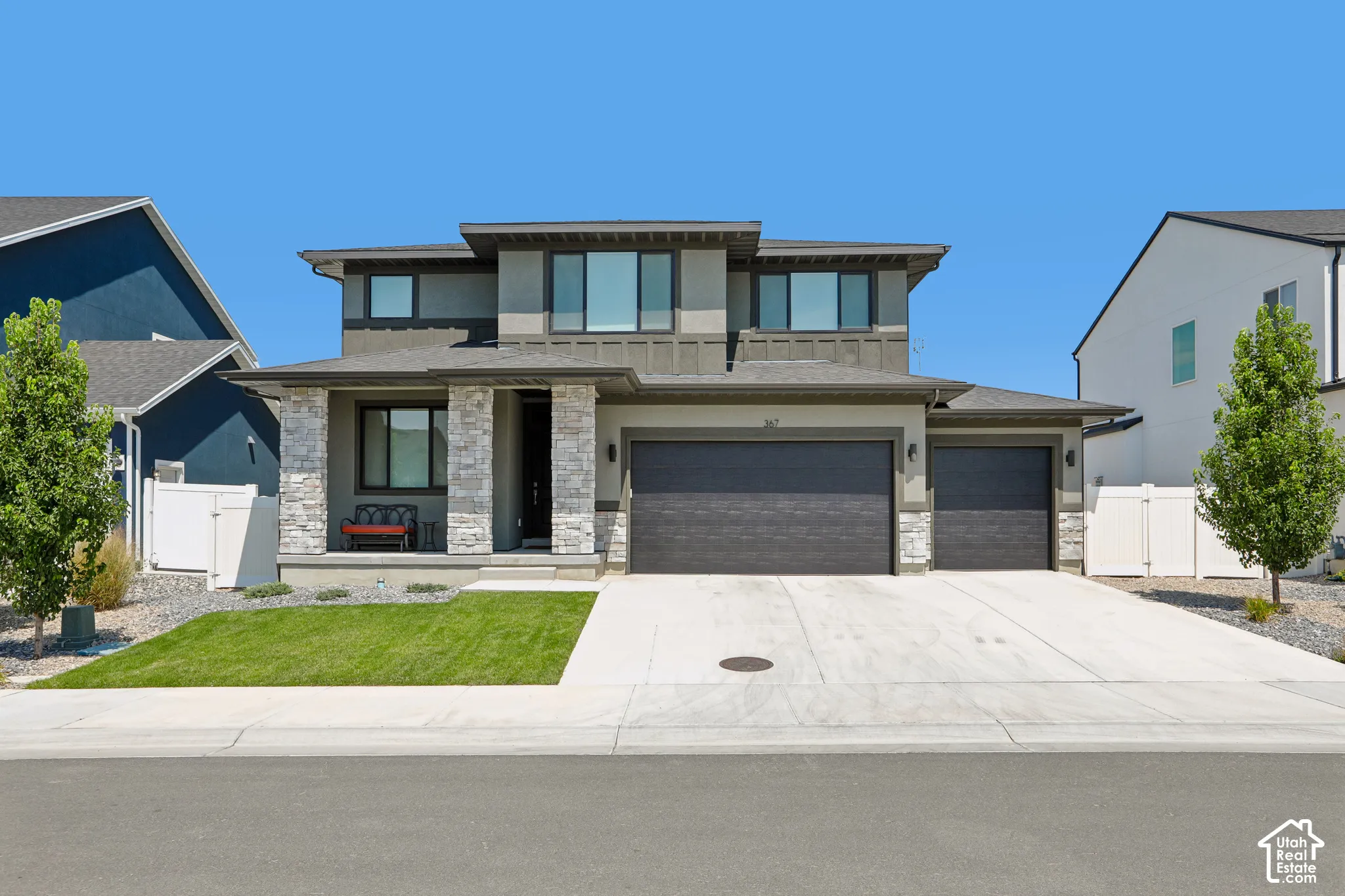 Contemporary two-story exterior featuring a stone and stucco facade, an attached two-car garage, a covered front entry, a concrete driveway, and a manicured lawn